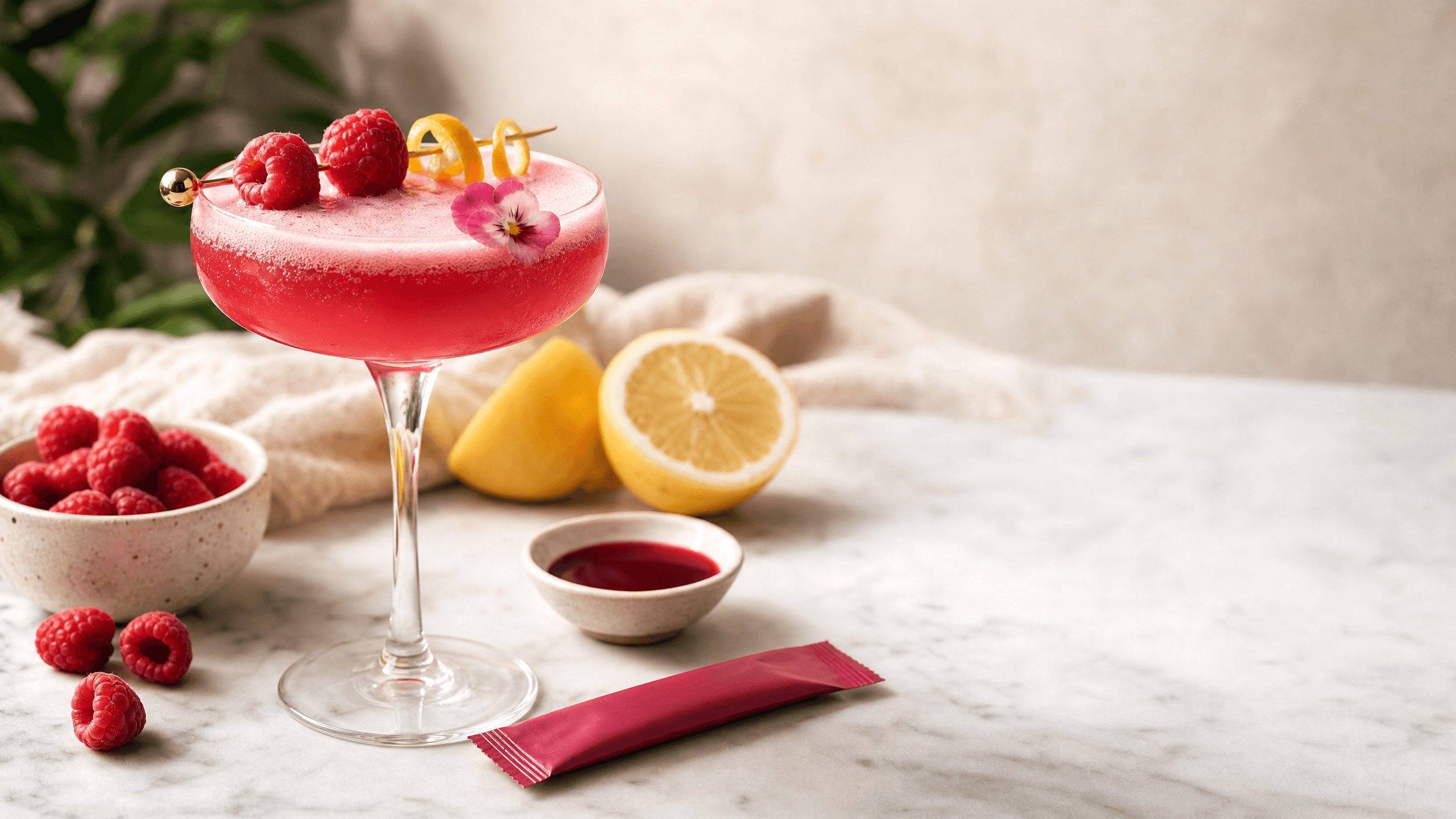 A bright raspberry kava fizz mocktail with lemon, berries, foam, and a KILA Raspberry Social Tonic on a clean bar surface